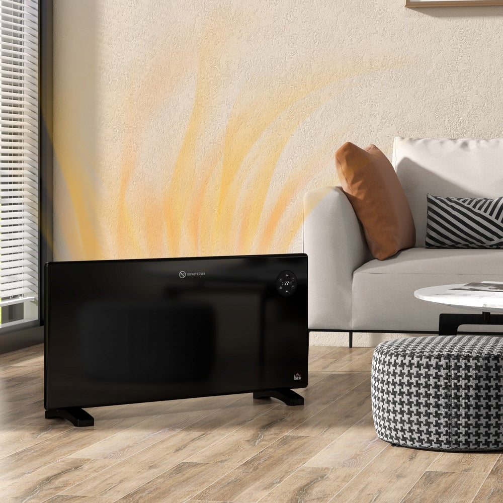 Black electric convector heater standing on a wooden floor in a modern living room next to a sofa