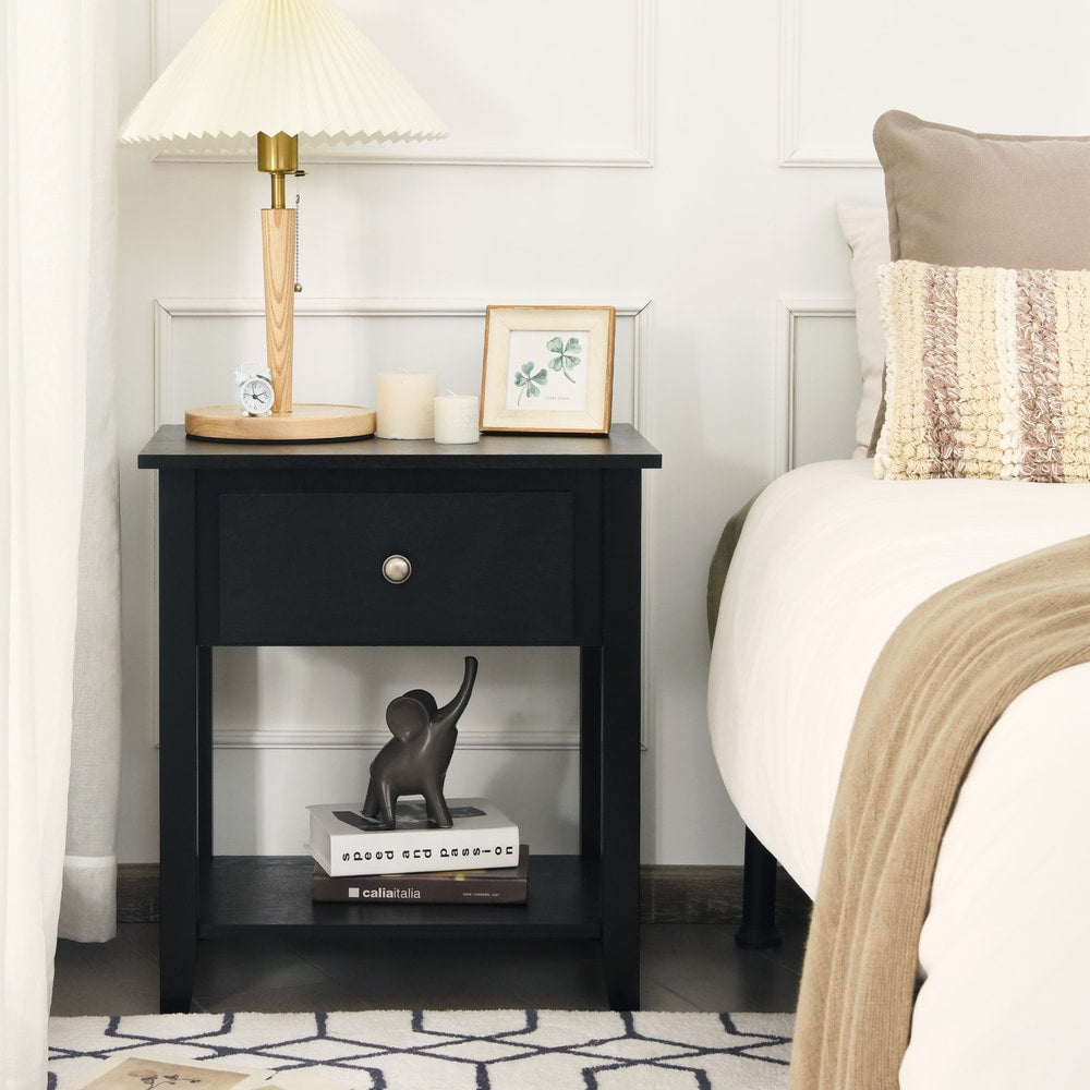 The black nightstand featuring a single drawer and open shelf beside a bed