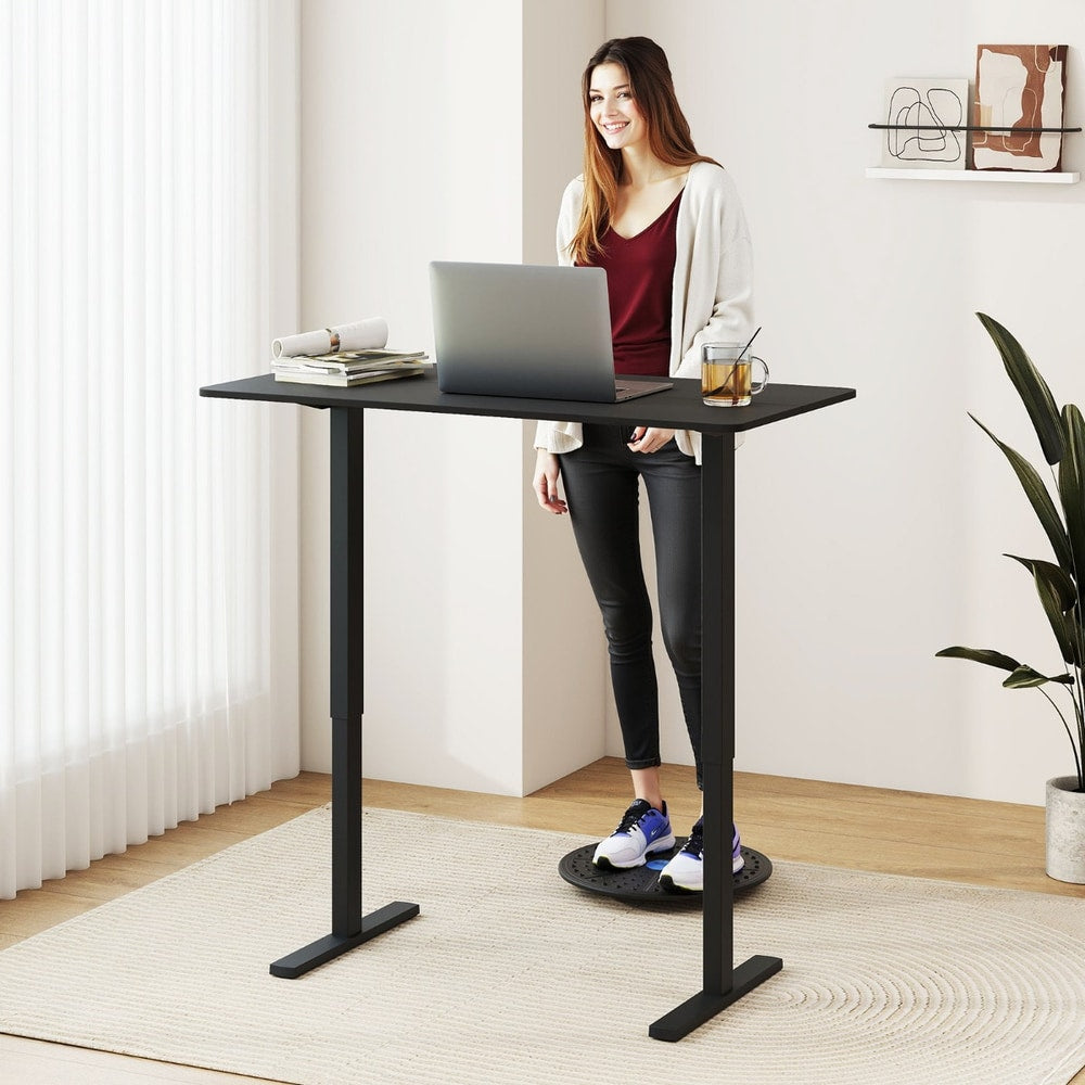 Woman using the black electric standing computer desk while standing on a balance board