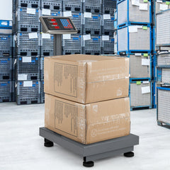 The kitchen scale with two cardboard boxes stacked on its platform in a warehouse setting