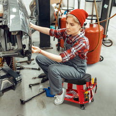 A person using the red rolling stool while working on a car in a garage setting