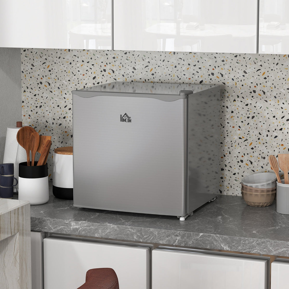 The grey mini freezer sits on a speckled kitchen counter next to canisters and utensils