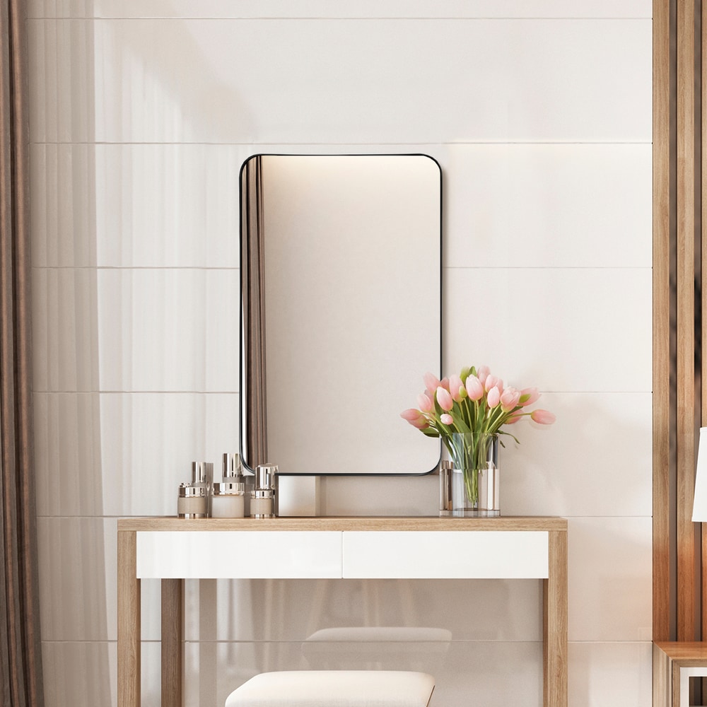 The bathroom mirror with rounded corners is shown above a vanity table with toiletries and flowers
