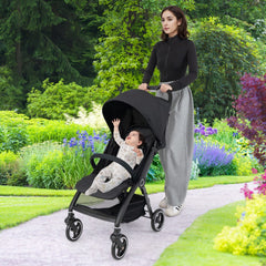 A woman pushes a baby in a black stroller along a garden path