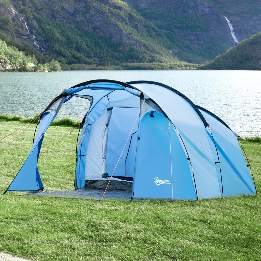 The camping tent set up on a grassy field by a lake with mountains in the background