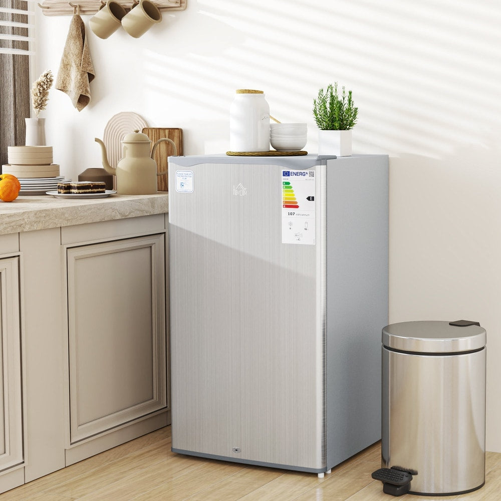 The compact fridge in a kitchen setting next to a bin and some kitchenware