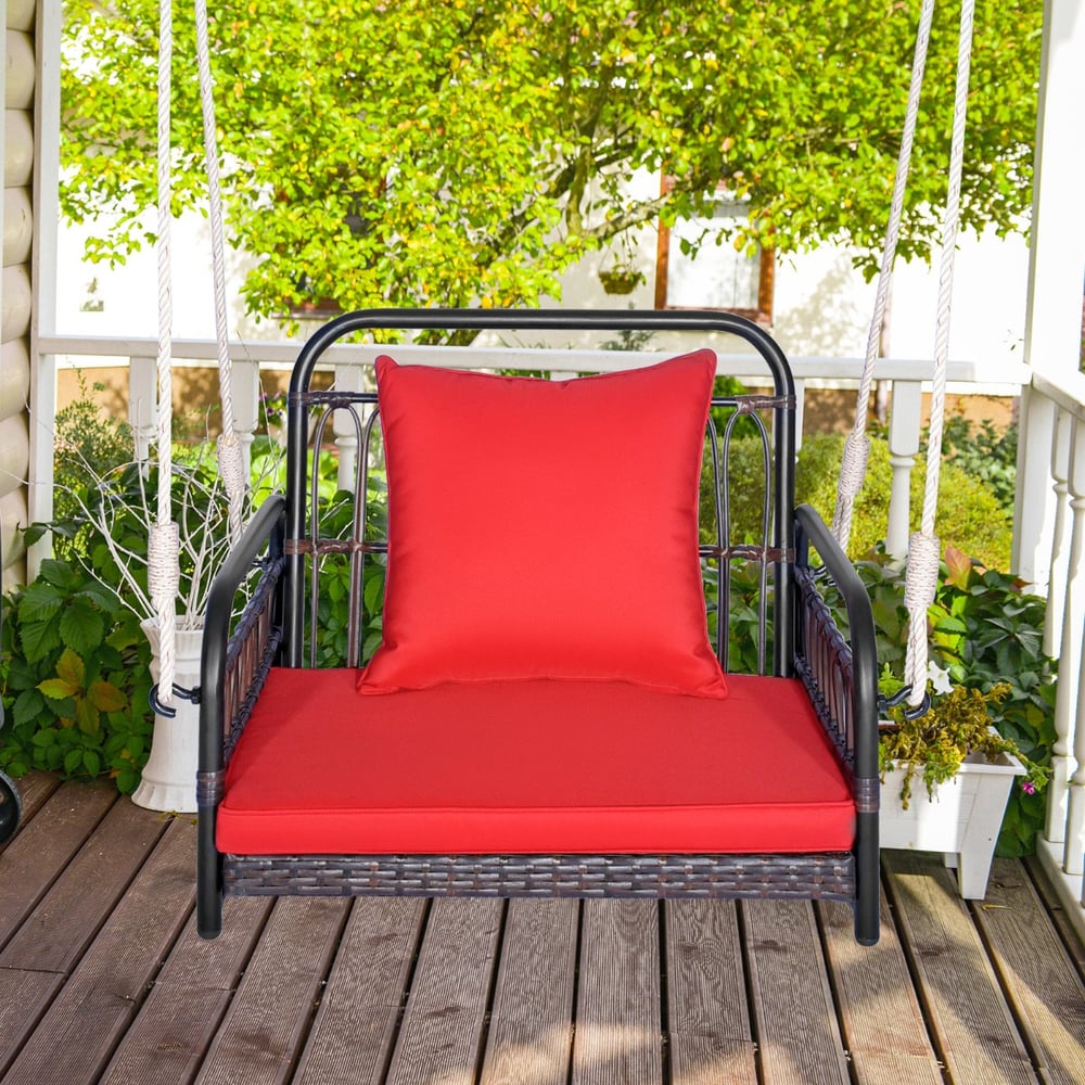 Red cushioned porch swing chair hanging on a wooden porch with green trees in the background