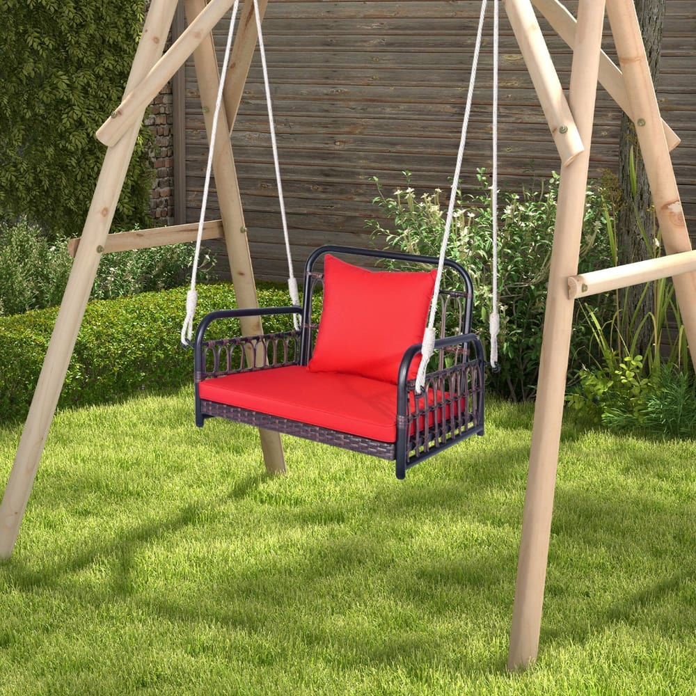 Red cushioned porch swing chair hanging from a wooden frame in a grassy garden