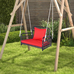Red cushioned porch swing chair hanging from a wooden frame in a grassy garden