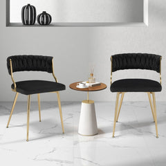 Two black velvet dining chairs with gold metal legs placed either side of a small round table