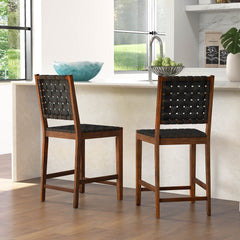 Two woven bar stools with black faux leather straps placed at a kitchen island