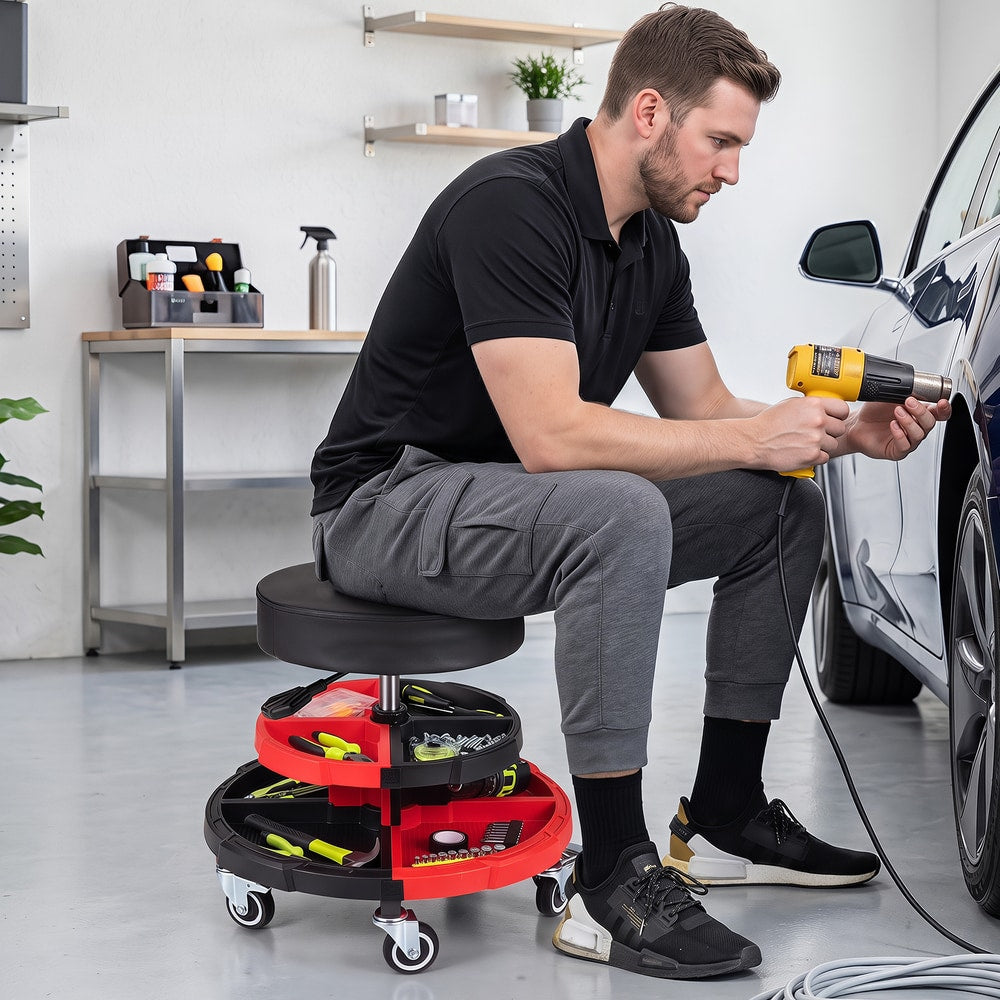 Man using the rolling stool and a heat gun on a car door