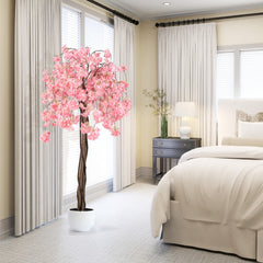 Artificial cherry blossom tree with pink flowers in a white pot beside a bed