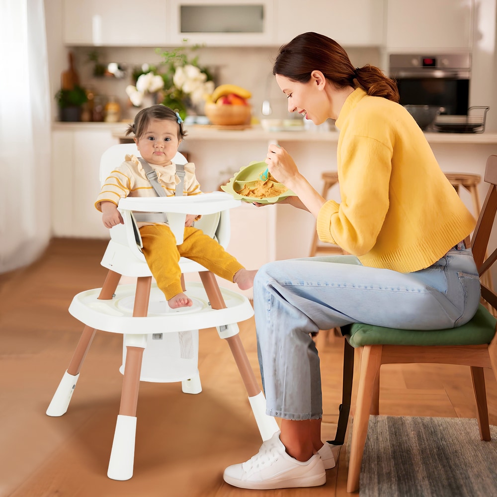 Mother feeding a baby in the white convertible high chair in a kitchen setting