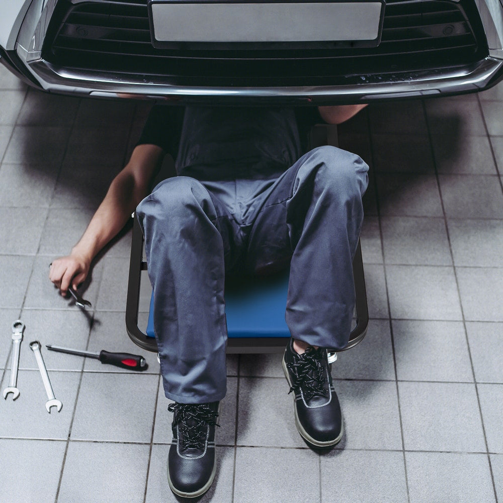 Mechanic using the blue rolling creeper seat under a car