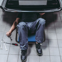 Mechanic using the blue rolling creeper seat under a car
