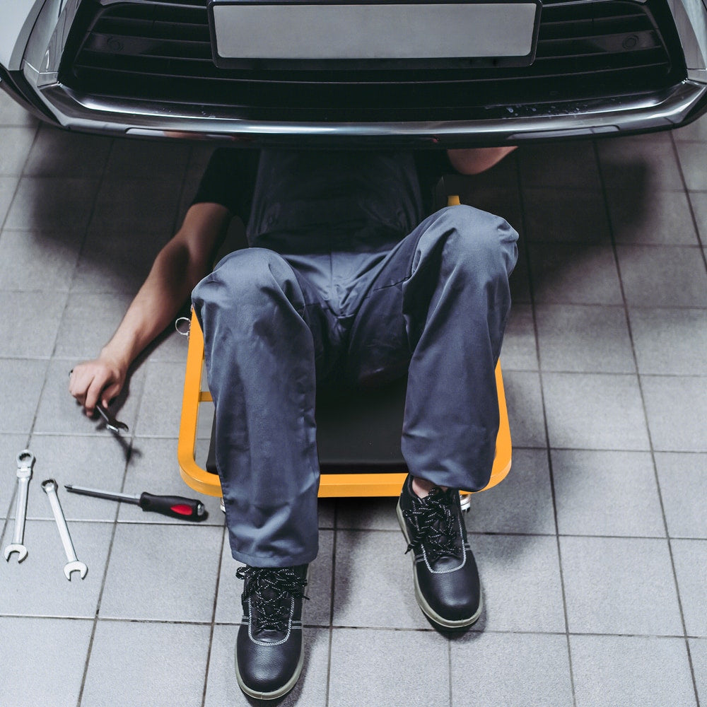 Mechanic lying on the floor using the rolling creeper seat under a car