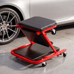 Red rolling creeper seat garage chair with black padding parked next to a car wheel