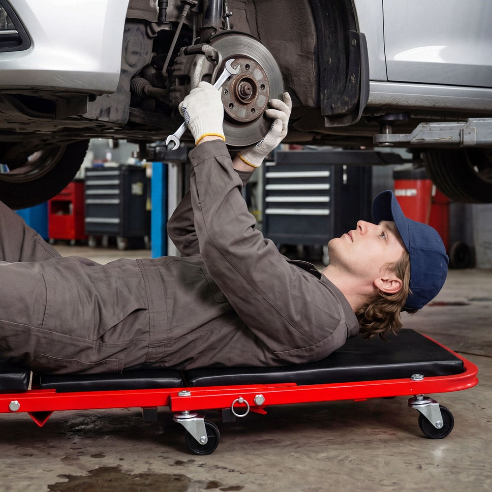 Man working on car wheel while lying on a red rolling creeper seat garage chair