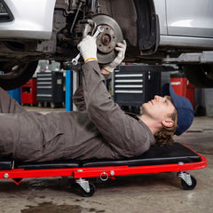 Man working on car wheel while lying on a red rolling creeper seat garage chair