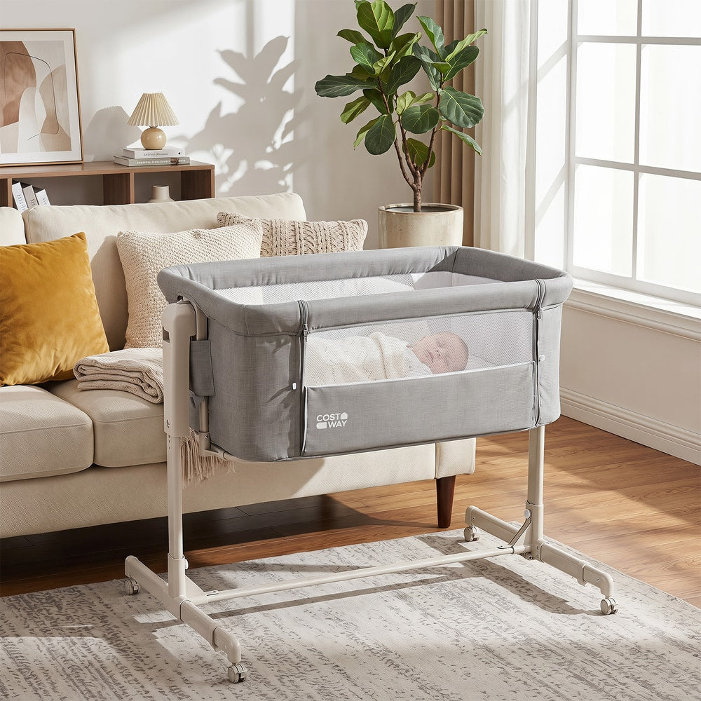 Grey bedside sleeper with a baby inside, next to a sofa