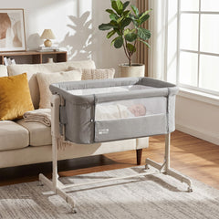 Grey bedside sleeper with a baby inside, next to a sofa