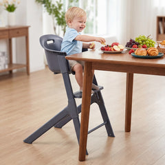 The high chair without a tray positioned at a dining table with a toddler eating fruit