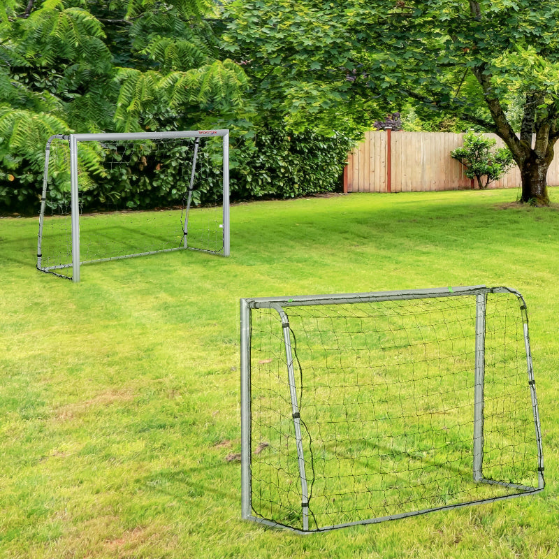 Two soccer goals on a grassy field with trees and a wooden fence in the background.