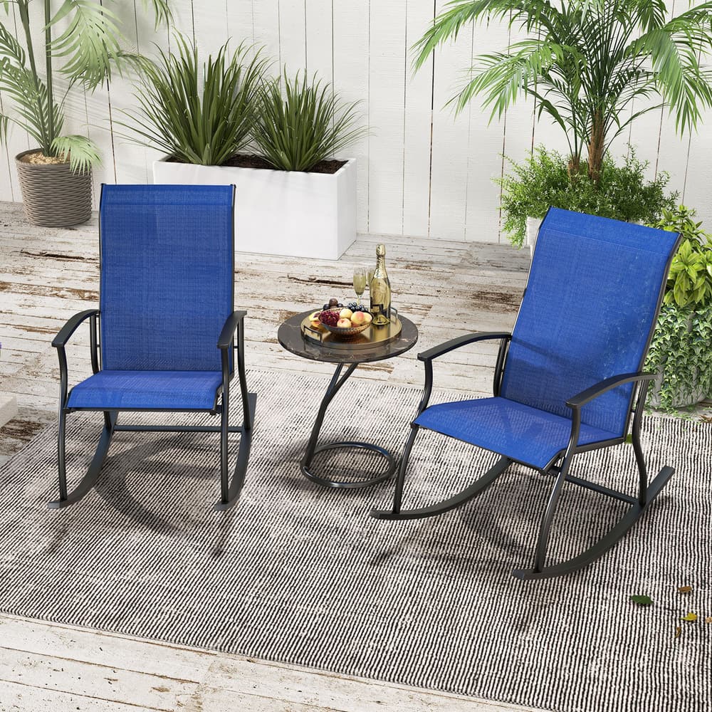 Two navy blue outdoor rocking chairs placed on a rug in a garden setting with a small table between them