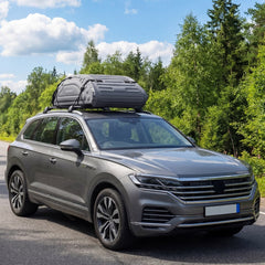 The grey foldable rooftop cargo carrier is attached to a car driving on a road