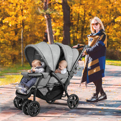 A woman pushes a grey double pushchair with two babies sitting in it outdoors