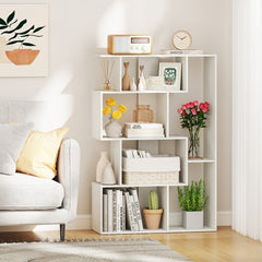 The white geometric bookcase styled with books, plants, and decorative items in a living room setting