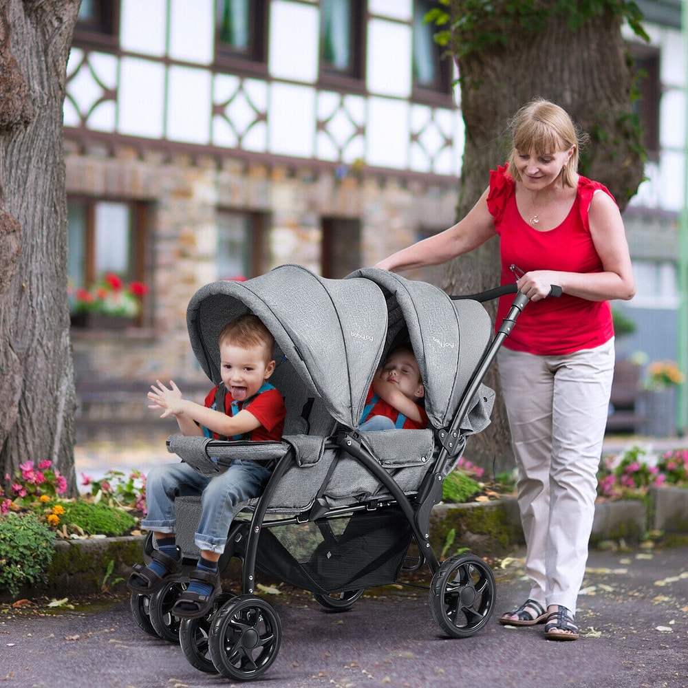 Two young boys sit in a grey double pushchair being pushed by a woman