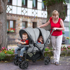 Two young boys sit in a grey double pushchair being pushed by a woman
