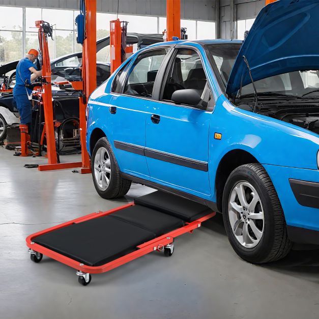 The rolling creeper seat being used under a blue car in a garage