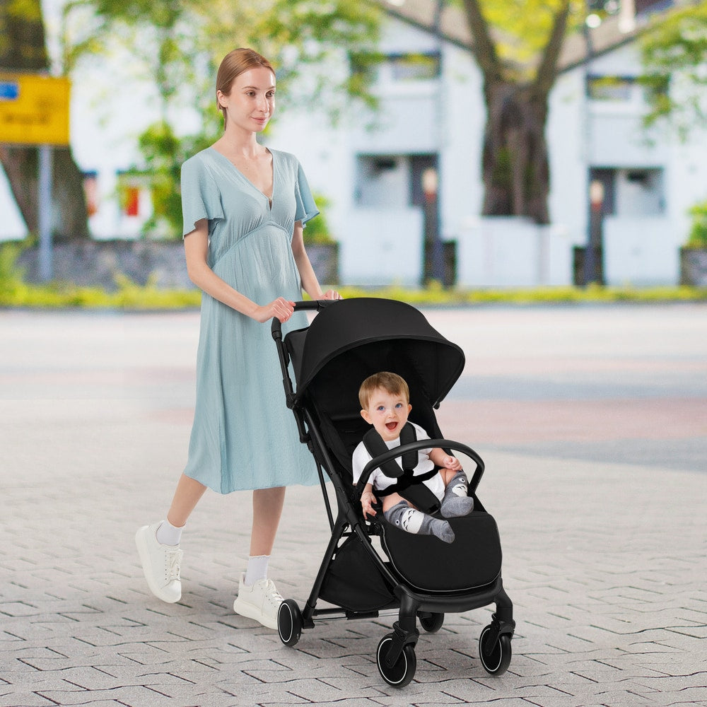 A woman pushing a black baby stroller with a baby sitting in it outdoors