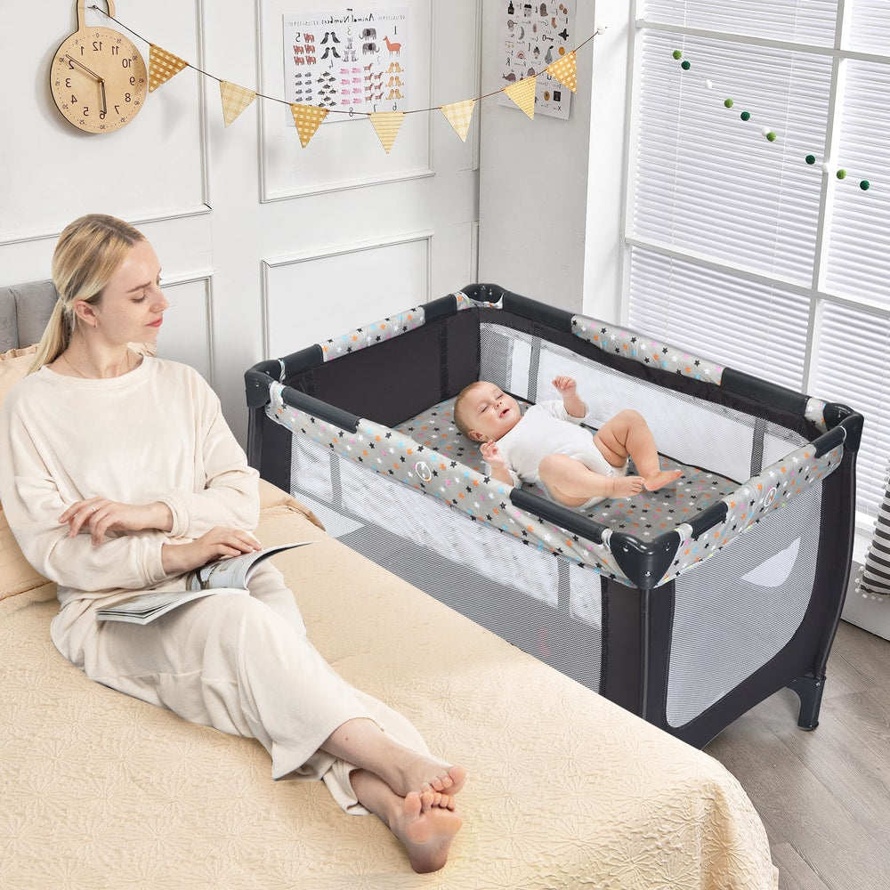The baby playpen placed next to a bed with a baby resting inside on the upper mattress level