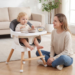 The high chair in use with a toddler sitting in a living room next to a woman