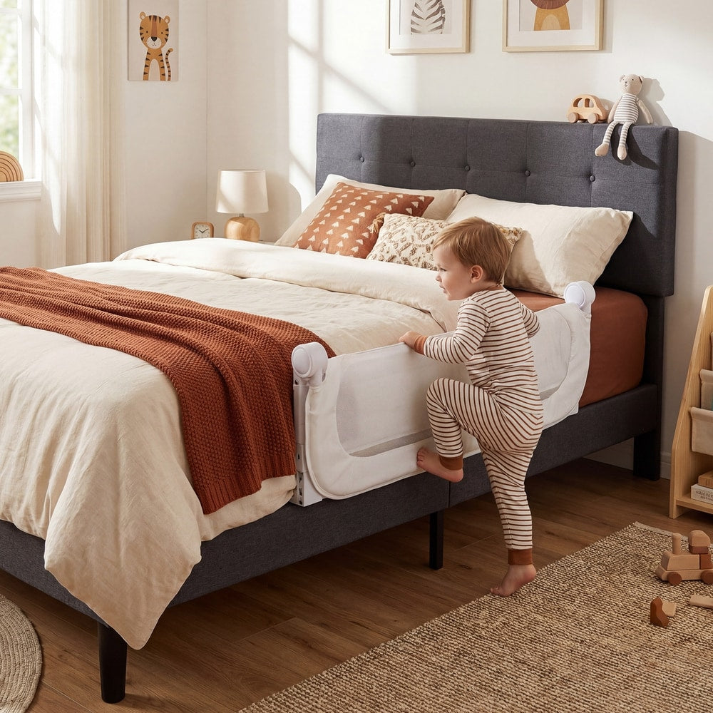 The bed rail secured to a grey upholstered bed as a toddler climbs into bed