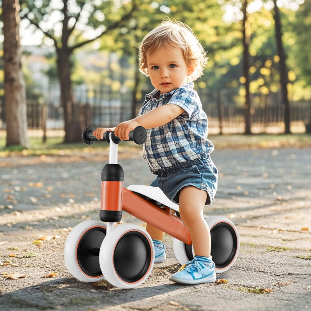 A happy toddler rides the orange balance bike outdoors on a paved path