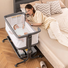 The bedside sleeper next to a bed with a baby inside and a woman lying down