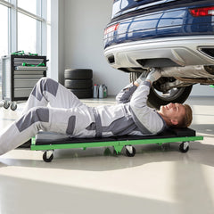 Mechanic lying on a green creeper under a car in a garage