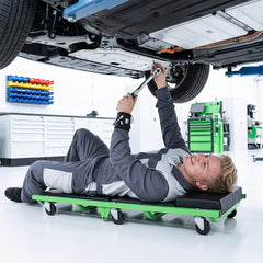 Man working on car underside while lying on a green creeper