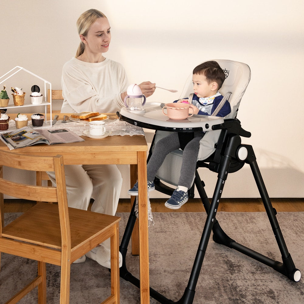 The high chair positioned next to a wooden dining table with a mother feeding her young child