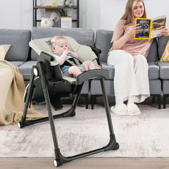 The high chair in a reclined position with a baby sitting in it while a woman reads nearby