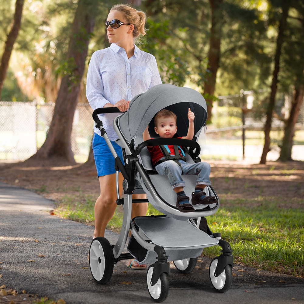 A woman pushing the grey baby stroller with a baby sitting in the seat
