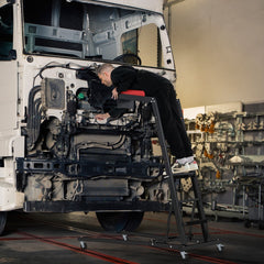 Mechanic working on a truck engine while lying on the automotive engine creeper