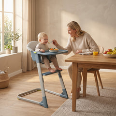 The high chair in use by a baby being fed by a woman at a wooden dining table