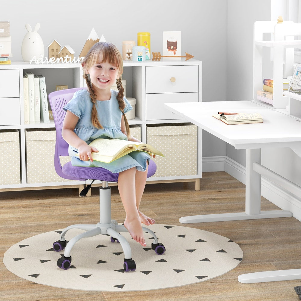 A young girl sitting on the purple kids study chair at a desk, reading a book