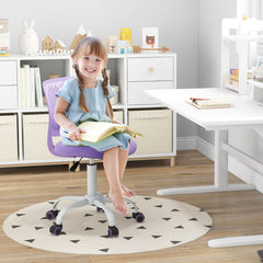 A young girl sitting on the purple kids study chair at a desk, reading a book